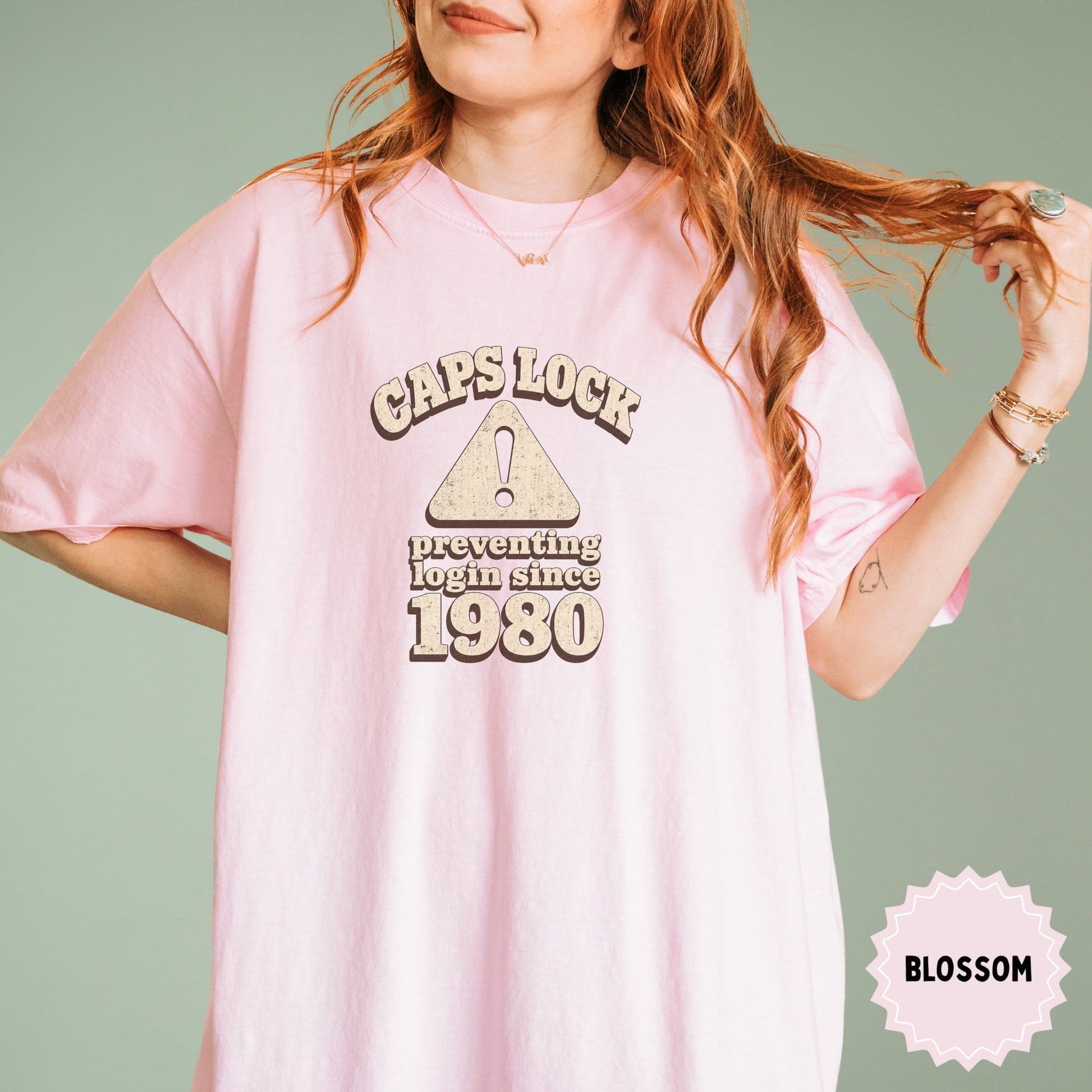 Pink t-shirt with "CAPS LOCK preventing login since 1980" text and warning symbol.