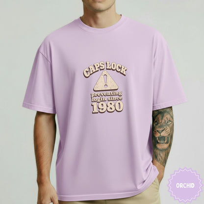 Lavender t-shirt with "Caps Lock preventing login since 1980" text and triangle warning sign.